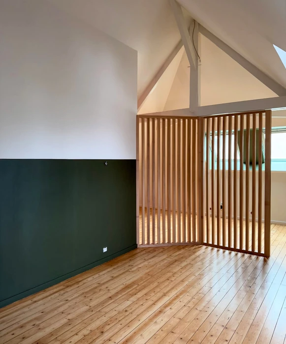 Espace intérieur vide sous combles rénovés, mur bicolore blanc/vert sapin à mi-hauteur, claustra en lamelles de bois naturel servant de séparation