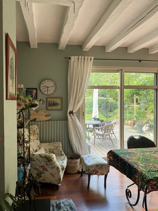 Salon lumineux avec murs vert sauge, poutres apparentes blanches, parquet en bois foncé