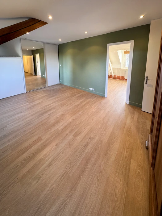 Pièce vide rénovée, sol en parquet stratifié ton chêne naturel, mur d'accent vert sauge mat, plafond blanc avec spots encastrés LED