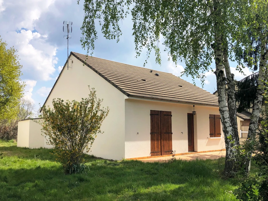 Maison plain-pied individuelle, façade enduit blanc, toiture à deux pans en tuiles terre cuite, volets et porte de garage battante en bois marron