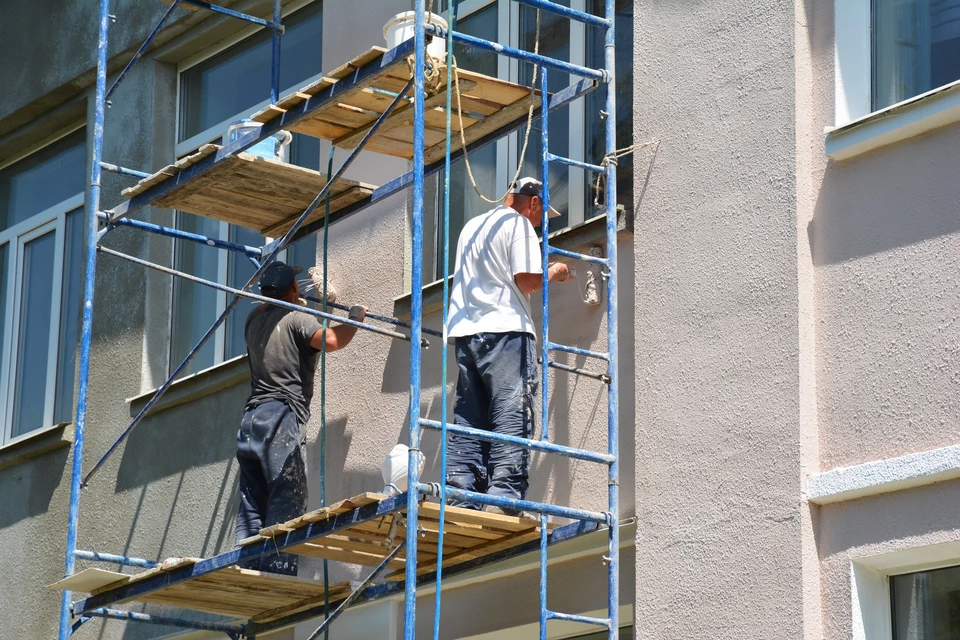 Des entrepreneurs peignent des murs extérieurs devant la façade de la maison