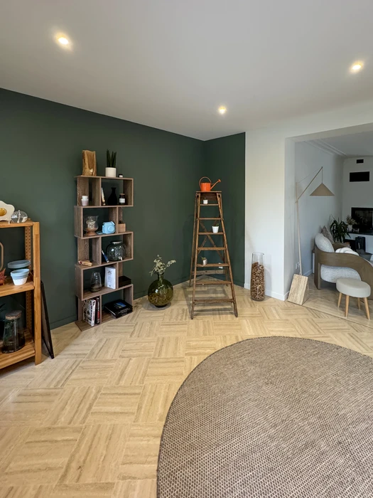 Intérieur rénovée d'une maison ancienne en pierre de taille, escalier droit en chêne massif avec garde-corps à barreaux verticaux, plafond avec poutres apparentes et lambris bois, sol en béton ciré gris, colonne en pierre calcaire, grande plante Dieffenbachia, rangement bas laqué blanc sous escalier, luminaires encastrés