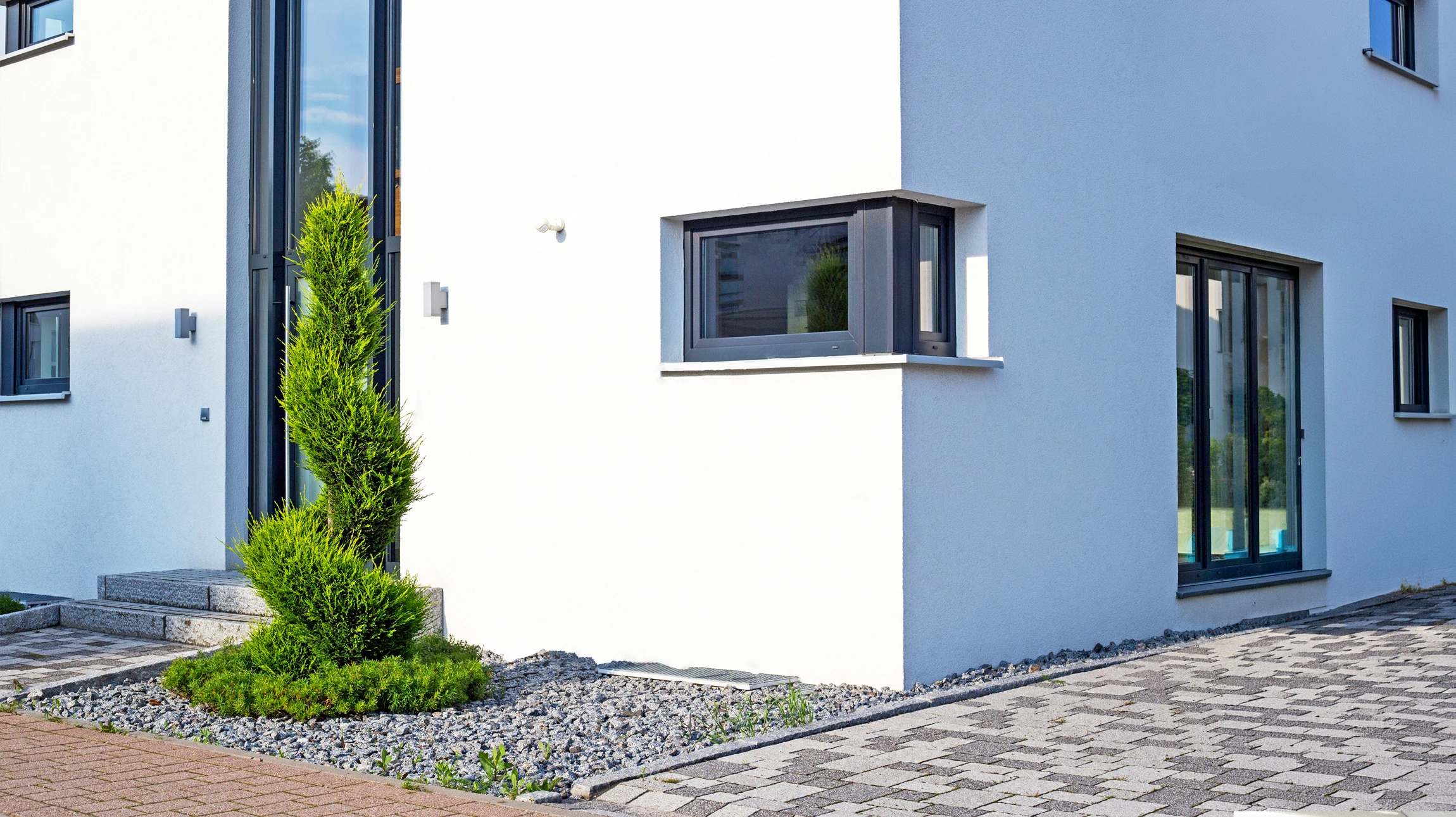 Ouvrier du bâtiment en vêtements de travail et casque blanc appliquant un enduit ou peinture blanche sur façade extérieure depuis échafaudage métallique